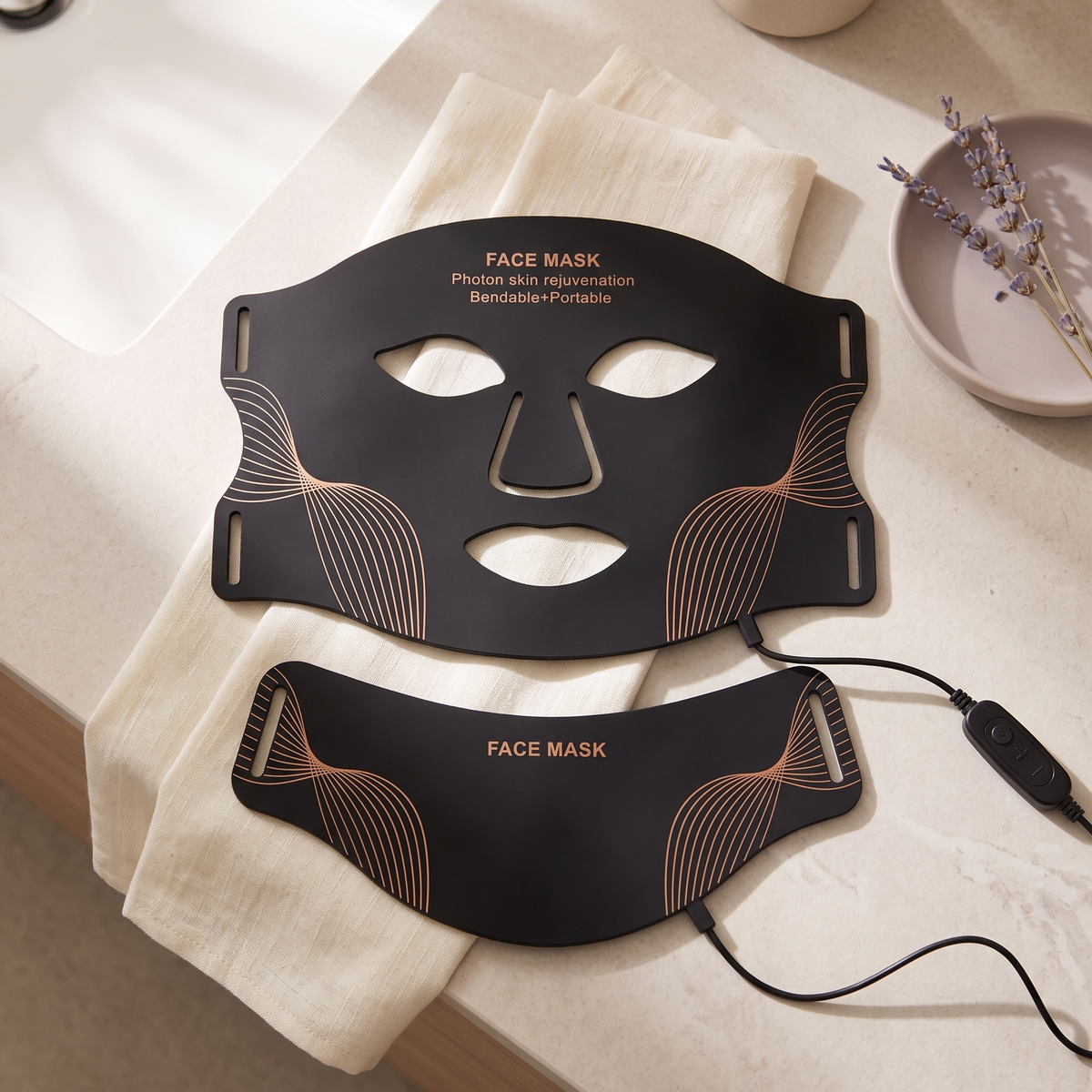 LED silicone face mask and neck piece laid flat on linen with the charging cable and controller
