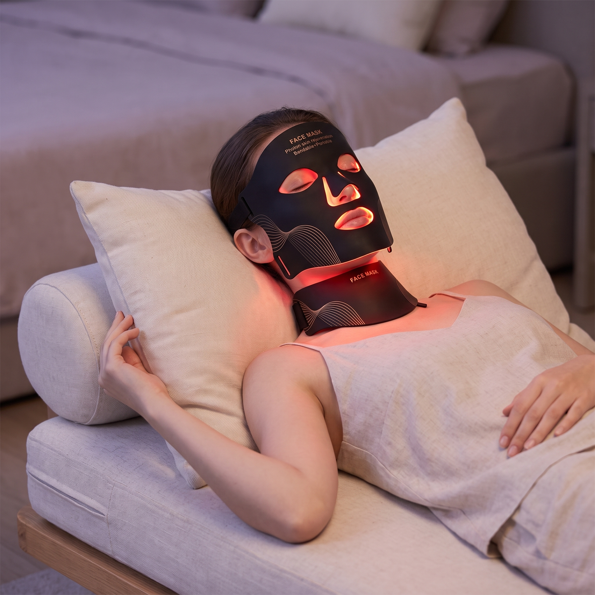 Woman reclining while wearing the LED silicone face and neck mask with the red light on